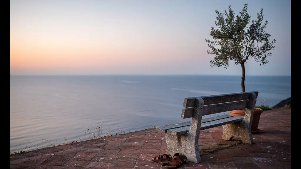 Vue large et minimaliste d'un banc vide face à un paysage méditerranéen épuré au crépuscule, symbolisant le besoin de pauses contemplatives pendant un voyage